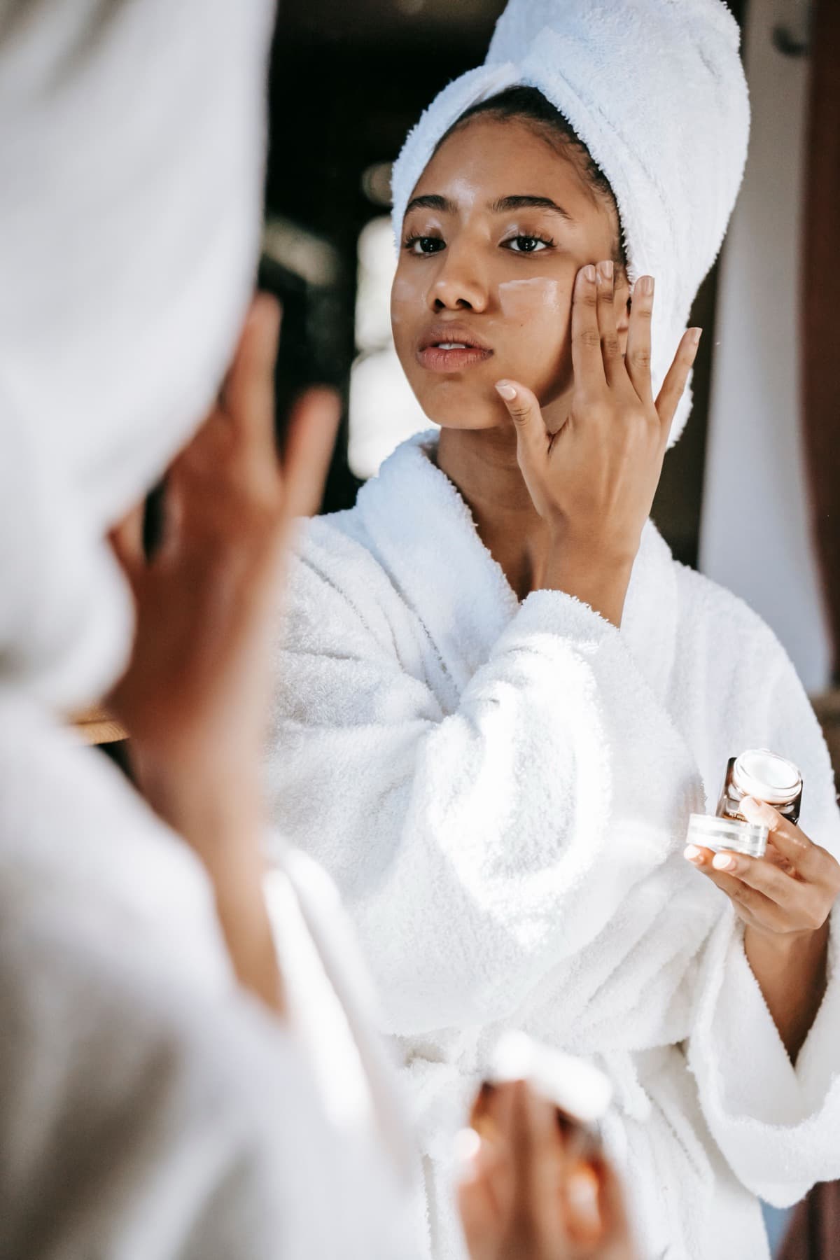 A woman applying moisturizer in a spa robe at a mirror